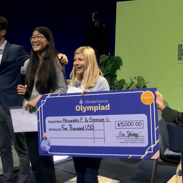 A group of people holding a big check, standing in front of a screen that says "UN CLIMATE CHANGE CONFERENCE UK 2021."