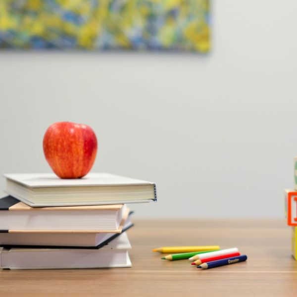 Image of an apple sitting on books on a desk with colored pencils.