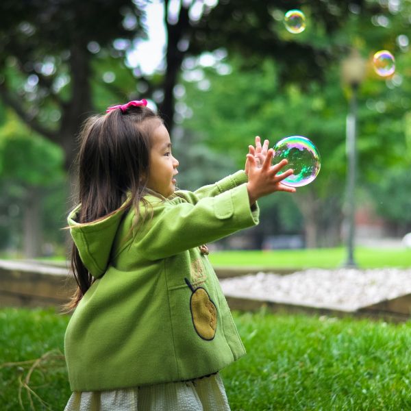 Child, wearing green, reaches for a bubble. 