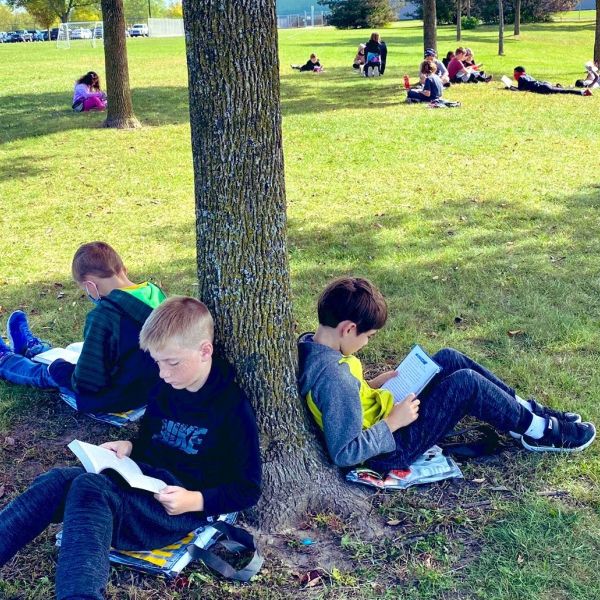 Students spread out sitting on "sit-upons" on a green lawn.