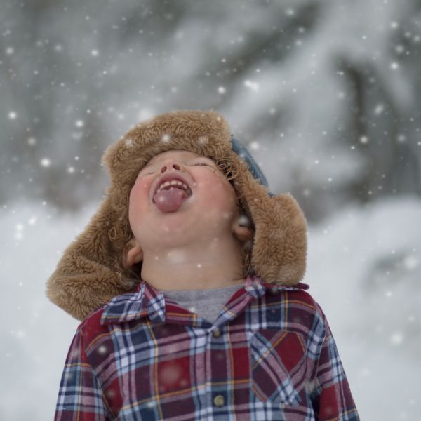 Photo of a young child facing the sky and trying to catch snowflakes