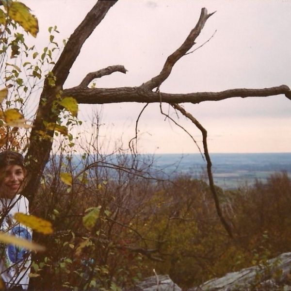 A younger Stacie standing amount trees on a rocky bluff.