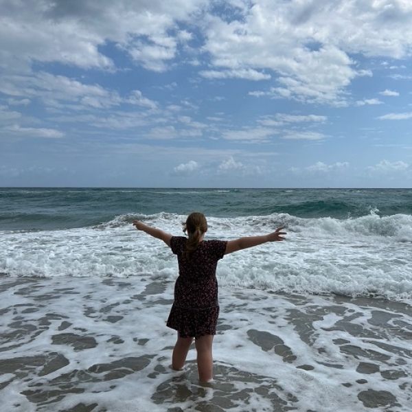 Girl with arms stretched towards the sky, standing in shallow waves in an ocean