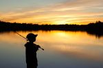 Silhouette of a young child holding a fishing pole and looking out at a body of water